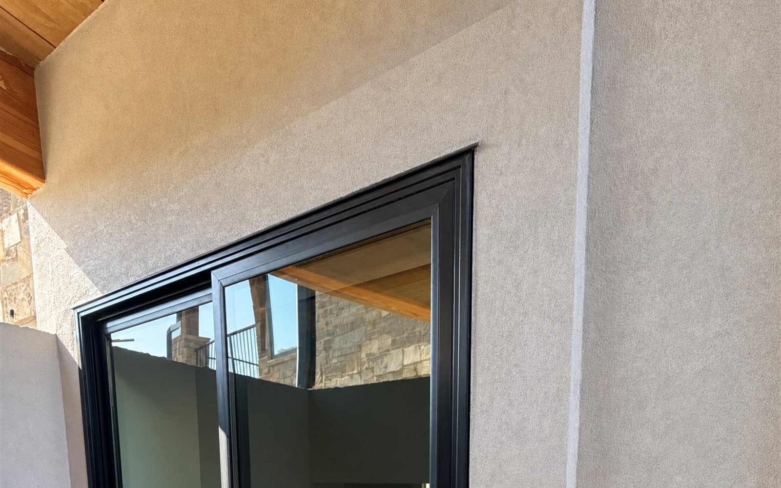 Smooth cream stucco finish beneath a wood soffit beside a black-framed window